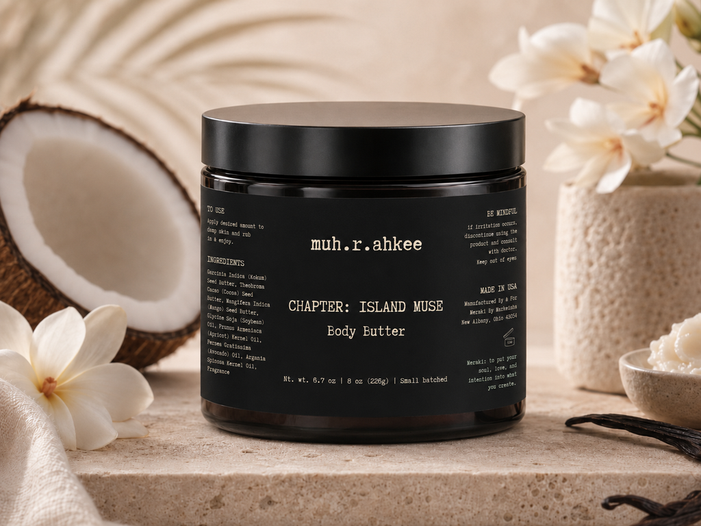 Black jar of 'muh.r.ahkee' Island Muse Body Butter with coconut and flowers in the background