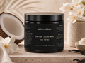 Black jar of 'muh.r.ahkee' Island Muse Body Butter with coconut and flowers in the background